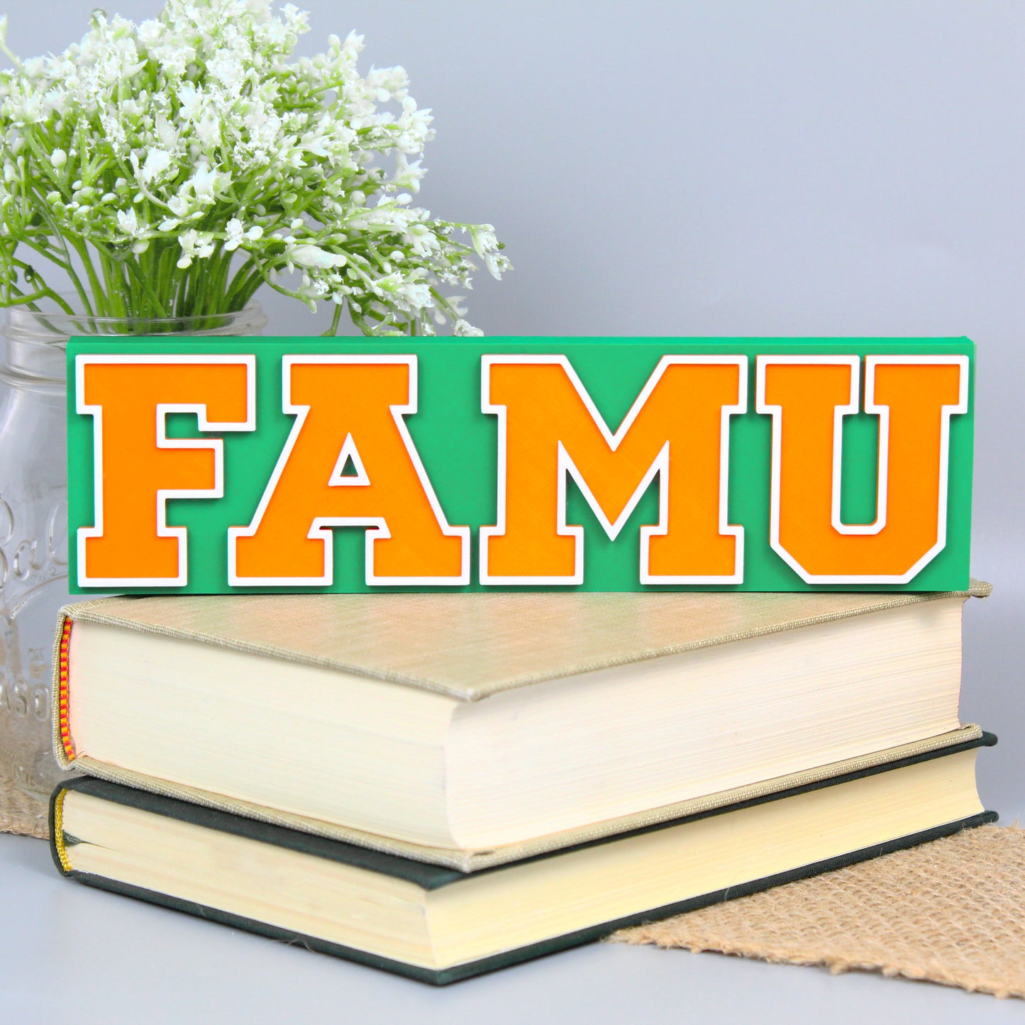 Florida A&M University decoration, green version, in front of a stack of books and mason jar with baby's breath flowers.