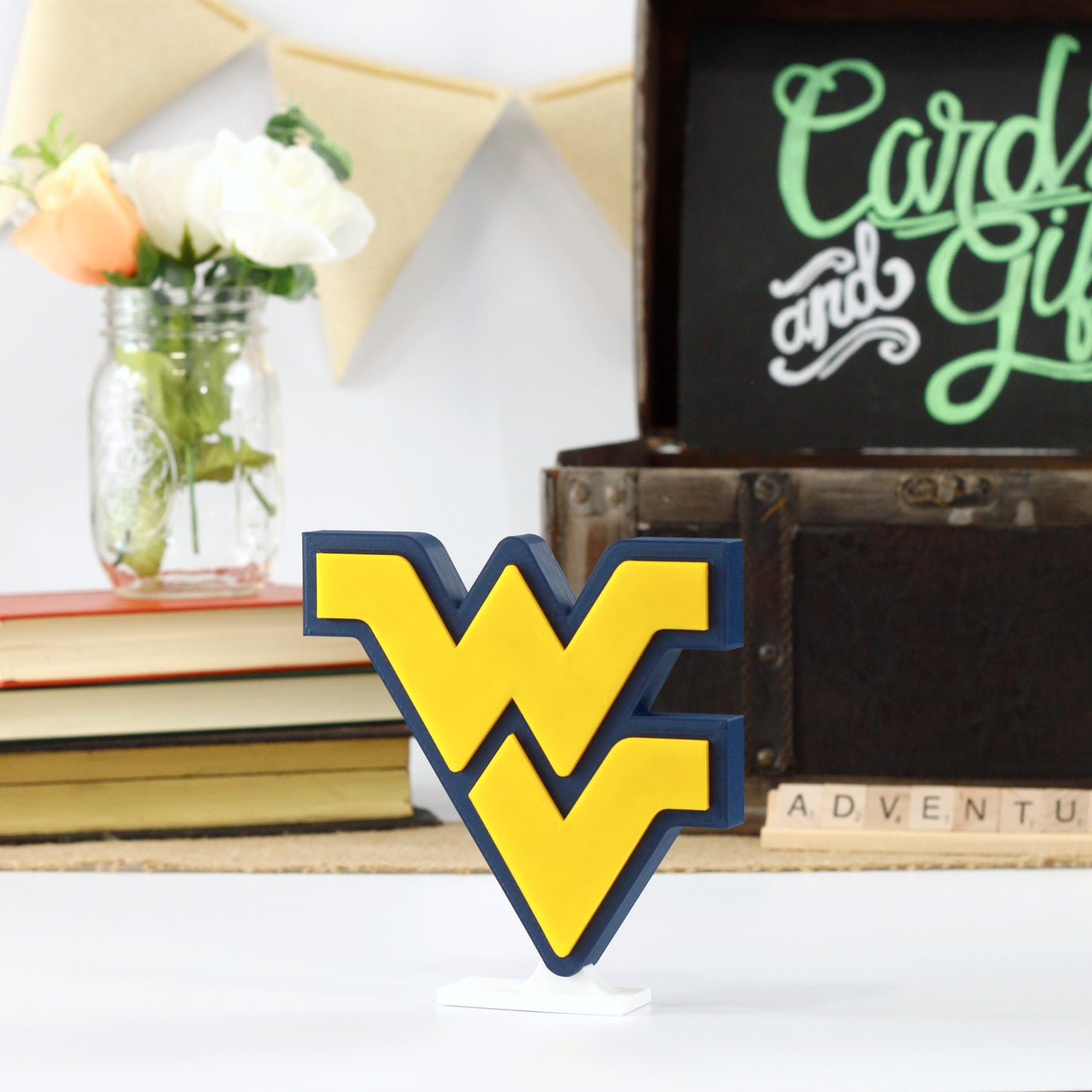 West Virginia University decoration in front of a stack of books and a chest for cards and gifts. Adventure in Scrabble titles.