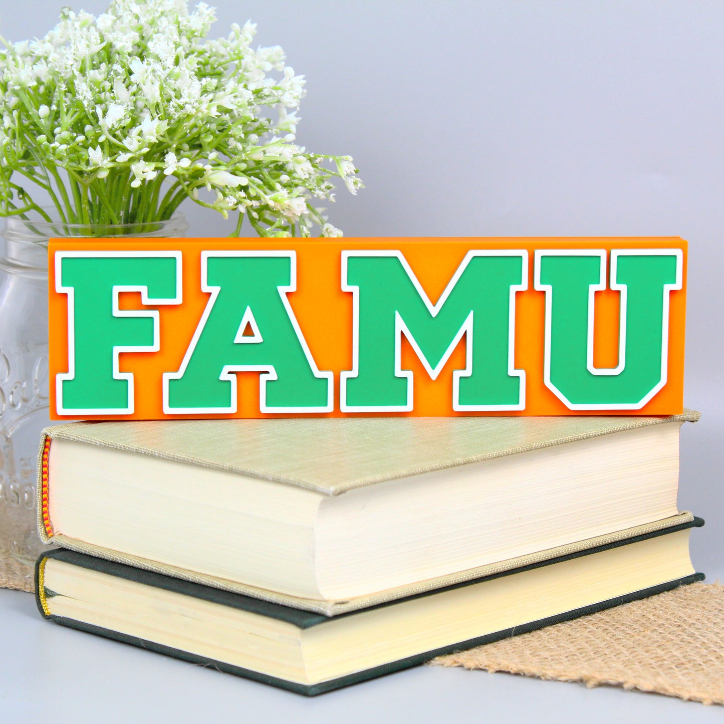 Florida A&M University decoration, orange version, in front of a stack of books and mason jar with baby's breath flowers.