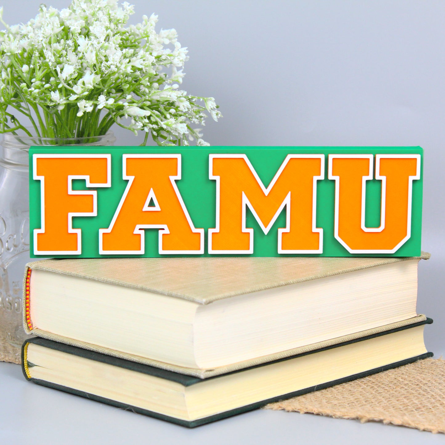 Florida A&M University decoration, green version, in front of a stack of books and mason jar with baby's breath flowers.