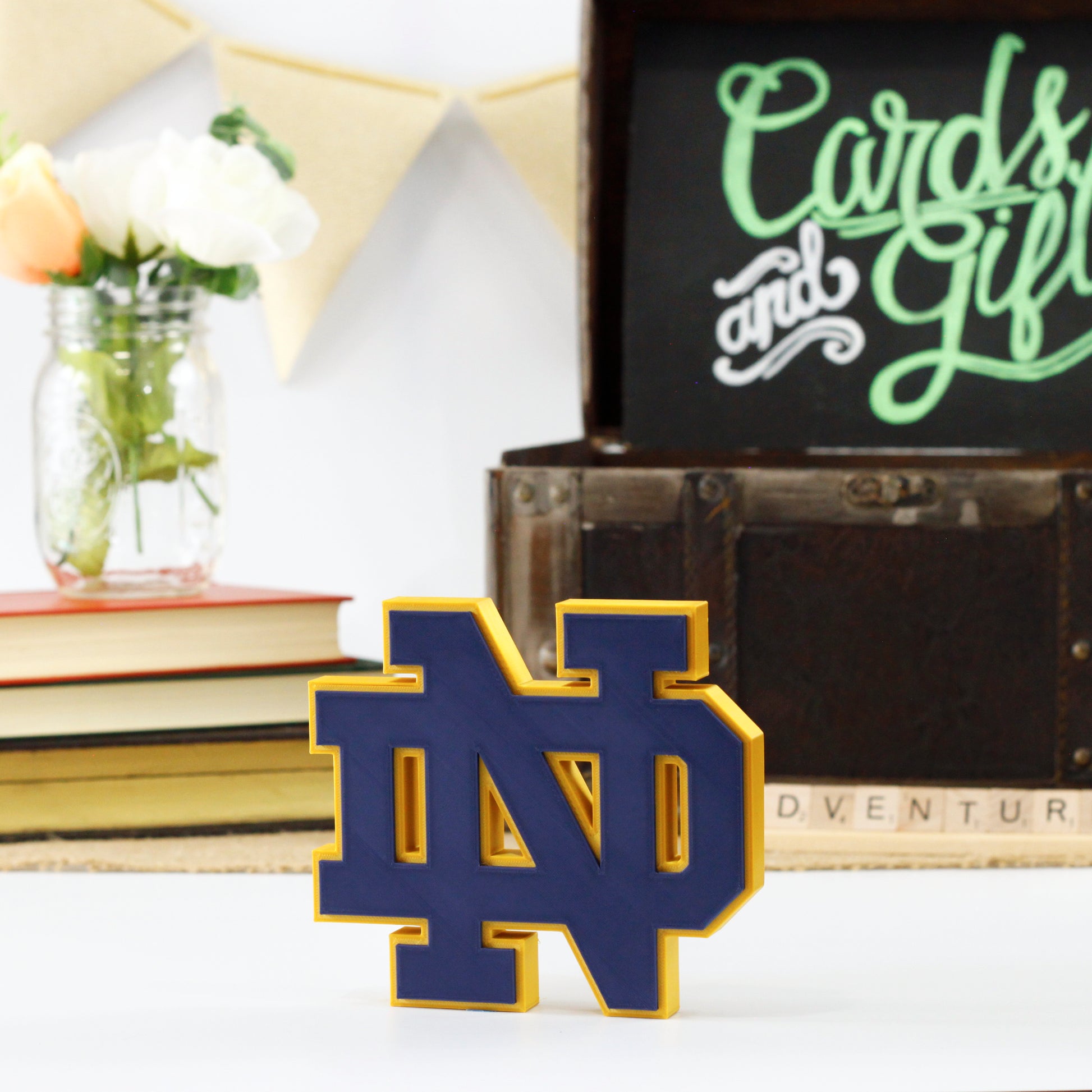University of Notre Dame decoration in front of a stack of books and a chest for cards and gifts. Adventure in Scrabble titles.