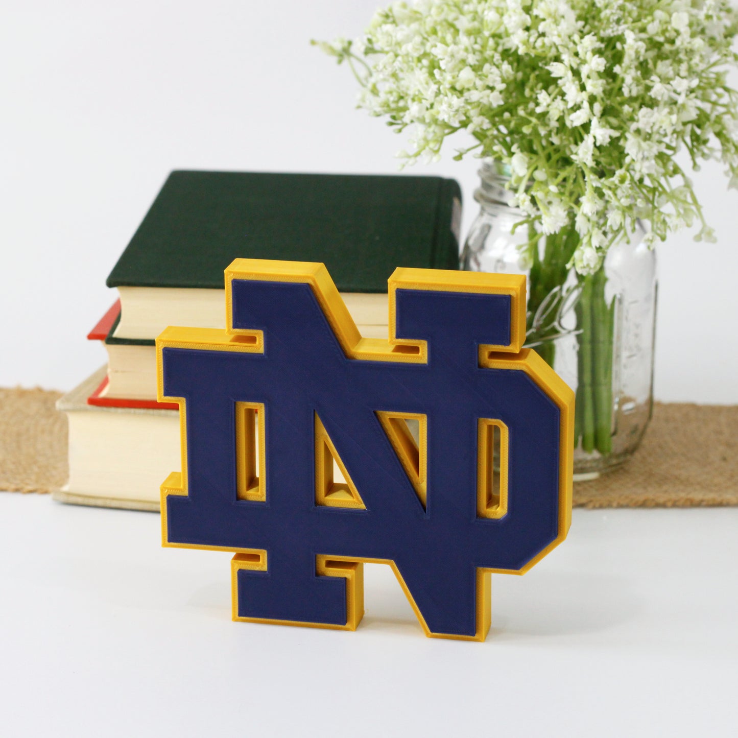 University of Notre Dame decoration in front of a stack of books and mason jar with baby's breath flowers.