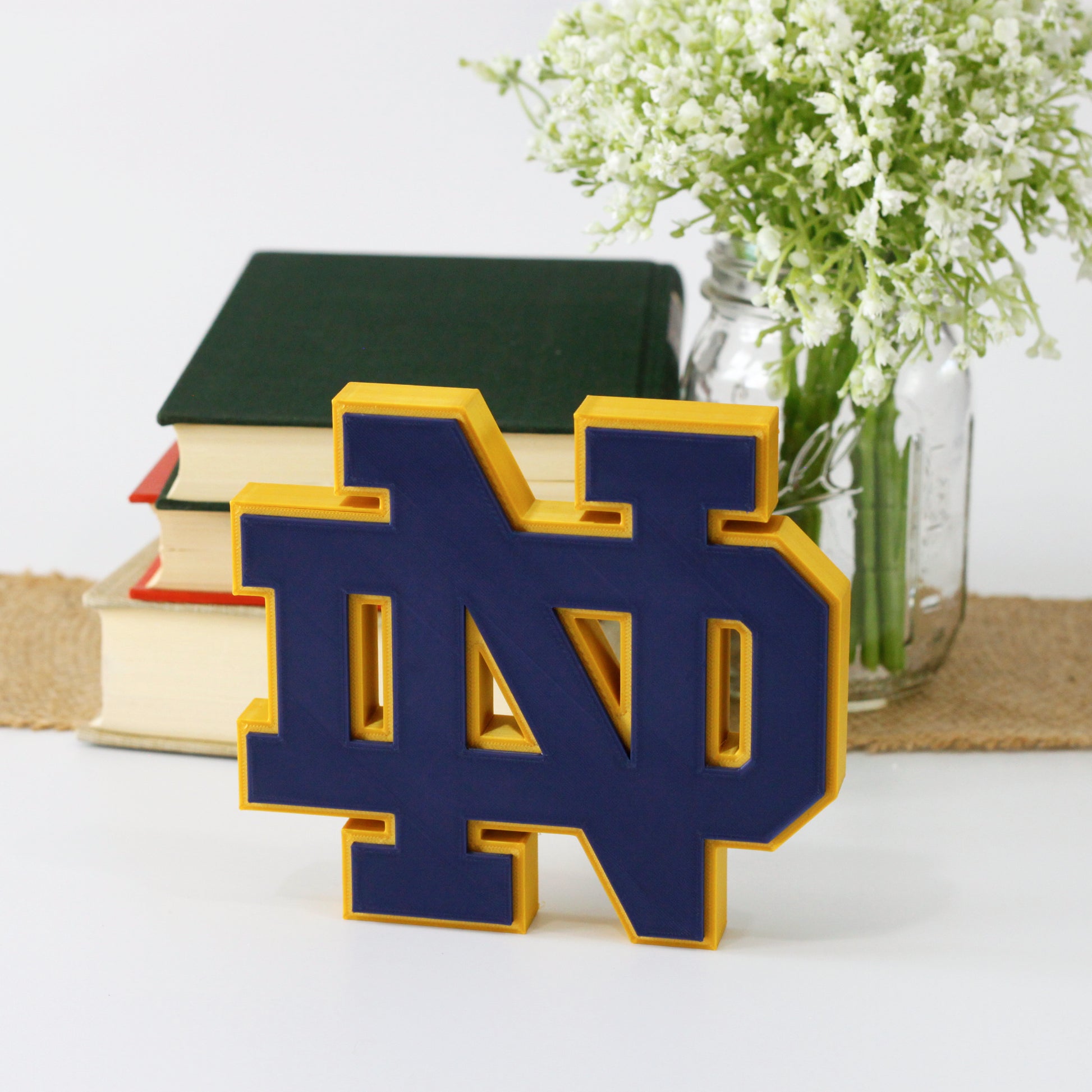 University of Notre Dame decoration in front of a stack of books and mason jar with baby's breath flowers.