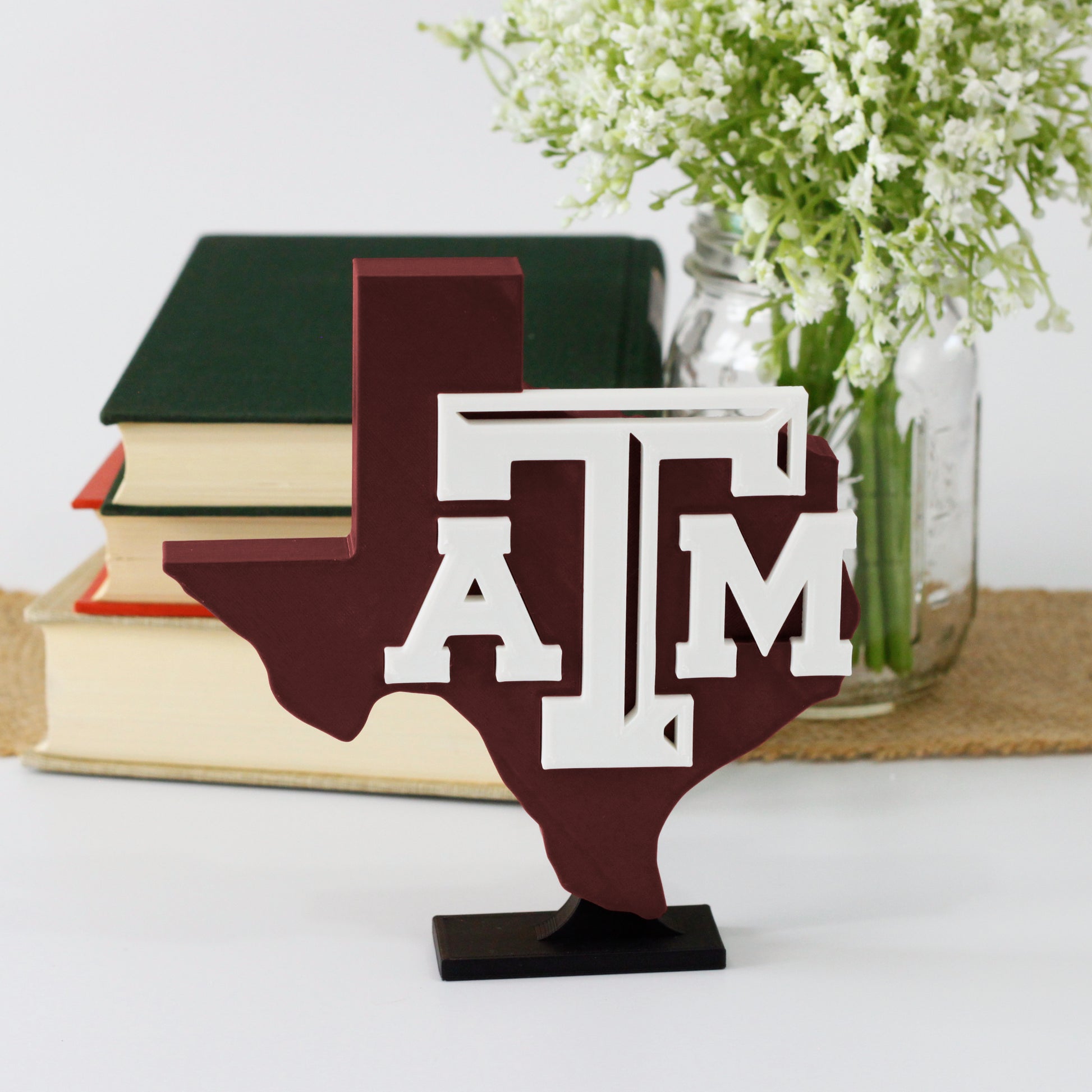 University of Texas A&M decoration in front of a stack of books and mason jar with baby's breath flowers.