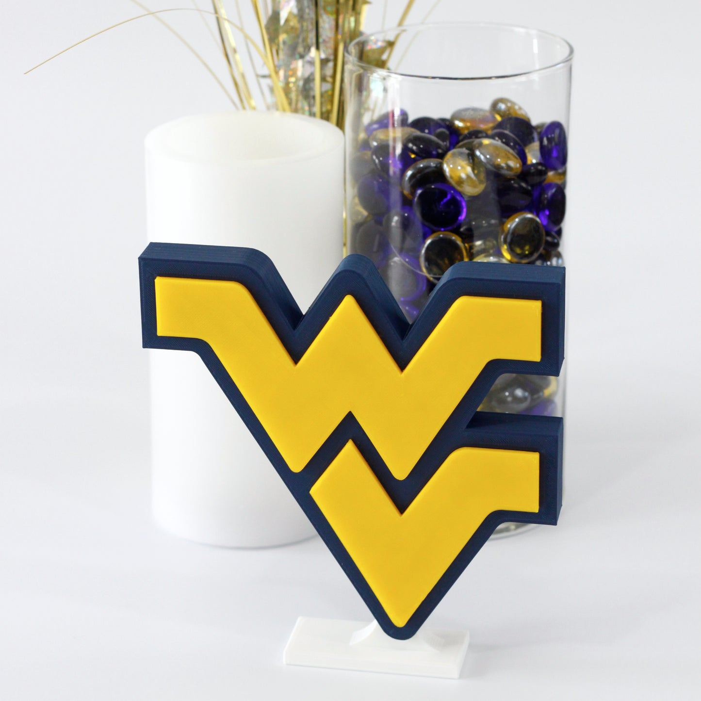 West Virginia University decoration in front of white candle, glass jar filled with colorful stones, and a silver and gold sparkler.
